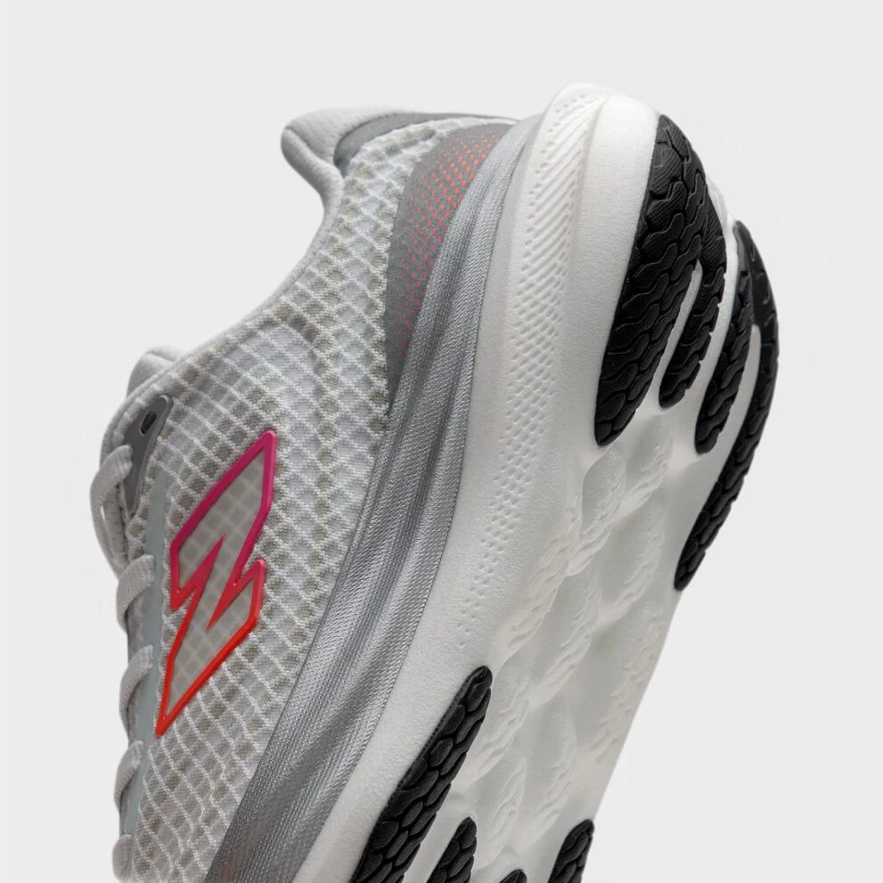Close‑up angled view of the heel and outsole of a light gray New Balance running shoe, showing textured mesh, layered midsole cushioning, black rubber tread pods, and a pink‑orange logo detail. 